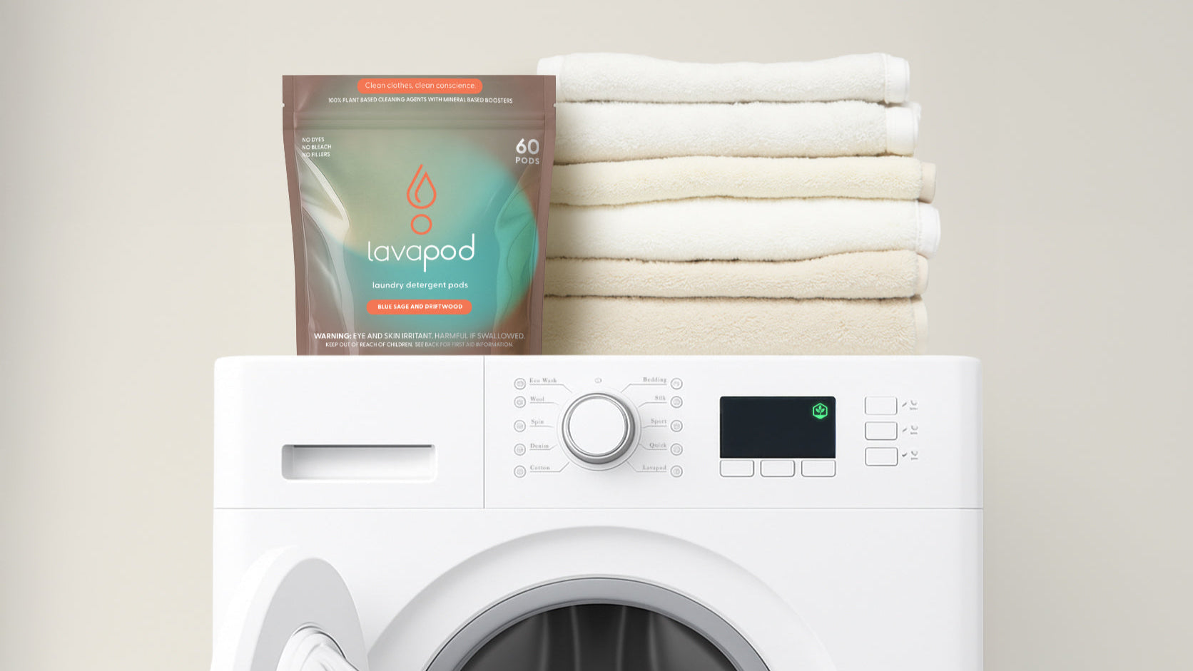 White washing machine with a stack of white towels and a Lavapod package on top against a beige wall.